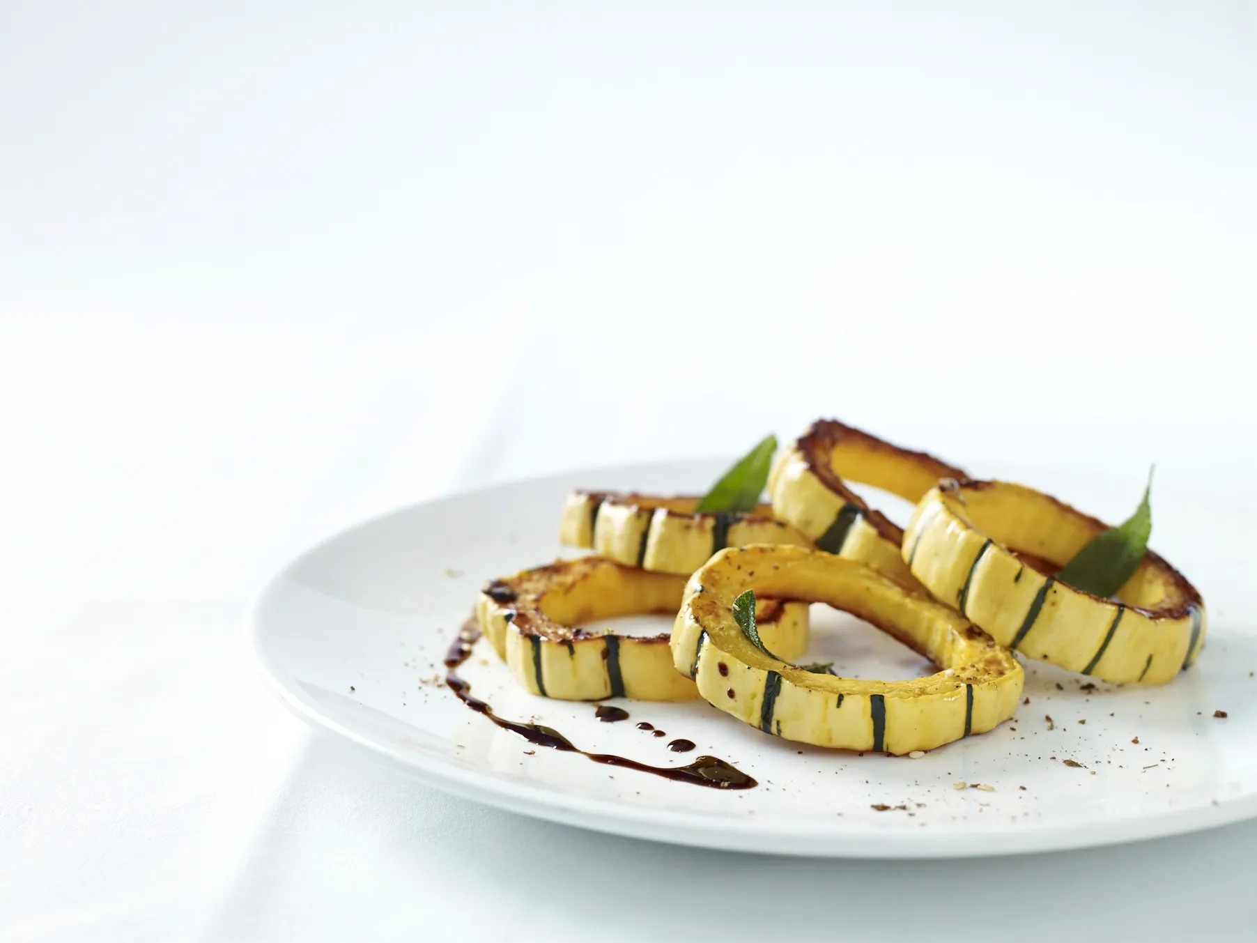 Grilled zucchini slices artfully plated with balsamic drizzle and garnish.