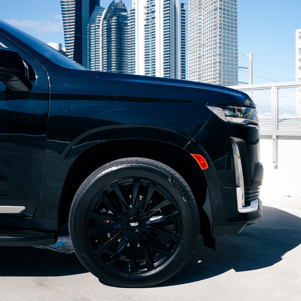 Side view of Escalade showing black wheels and tinted windows under bright sun