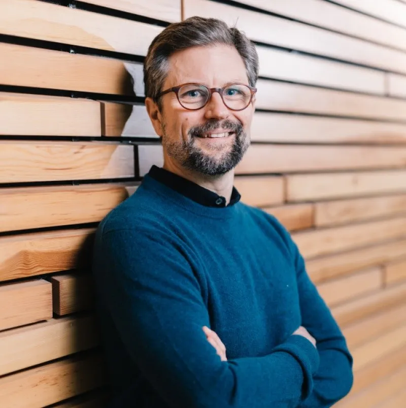 Ein Portraitfoto von Prof. Dr. Philipp Cimiano der vor einer Holzwand steht.