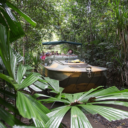 A group of people is riding an amphibious vehicle labeled "Rainforestation" through a dense, green tropical rainforest.