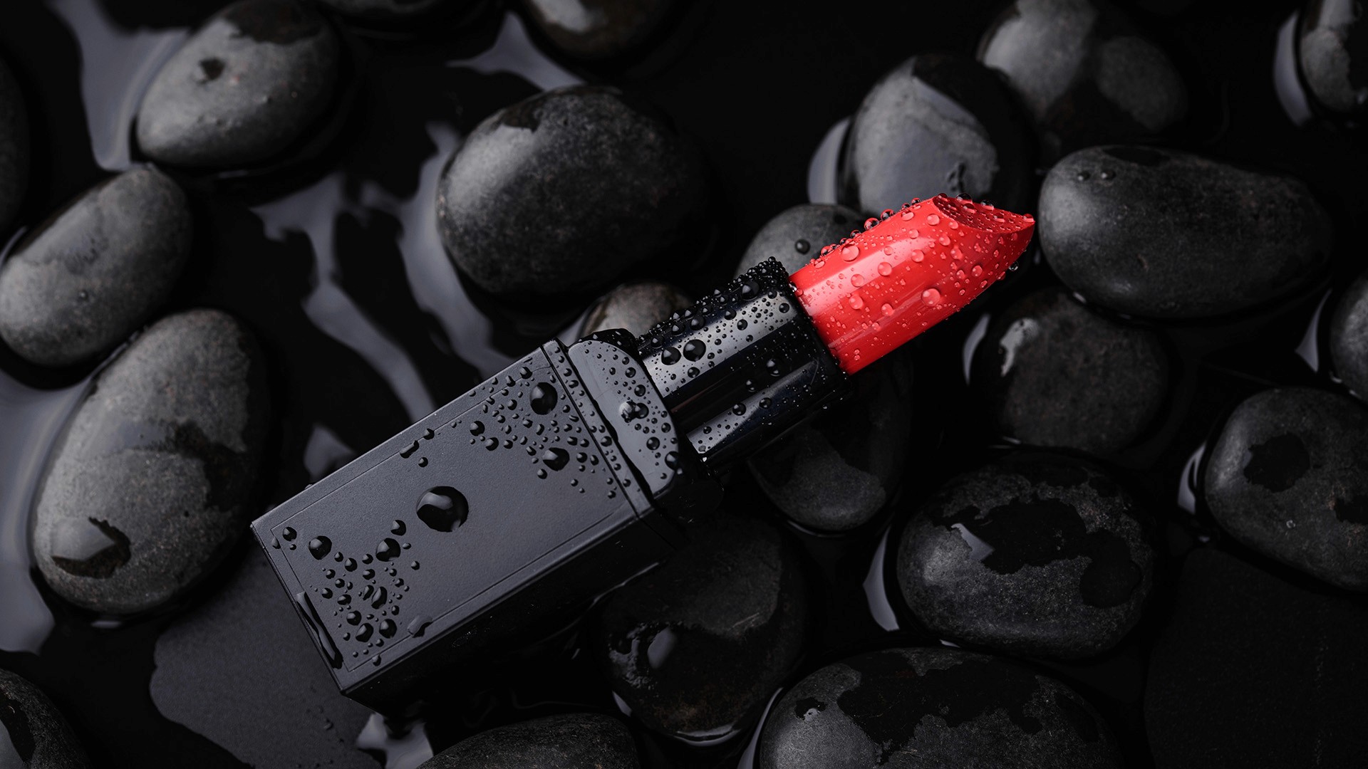 A vibrant red lipstick with water droplets is artfully placed on smooth black stones, showcasing a modern and sleek product photography style, aligning with the latest trends for 2026.