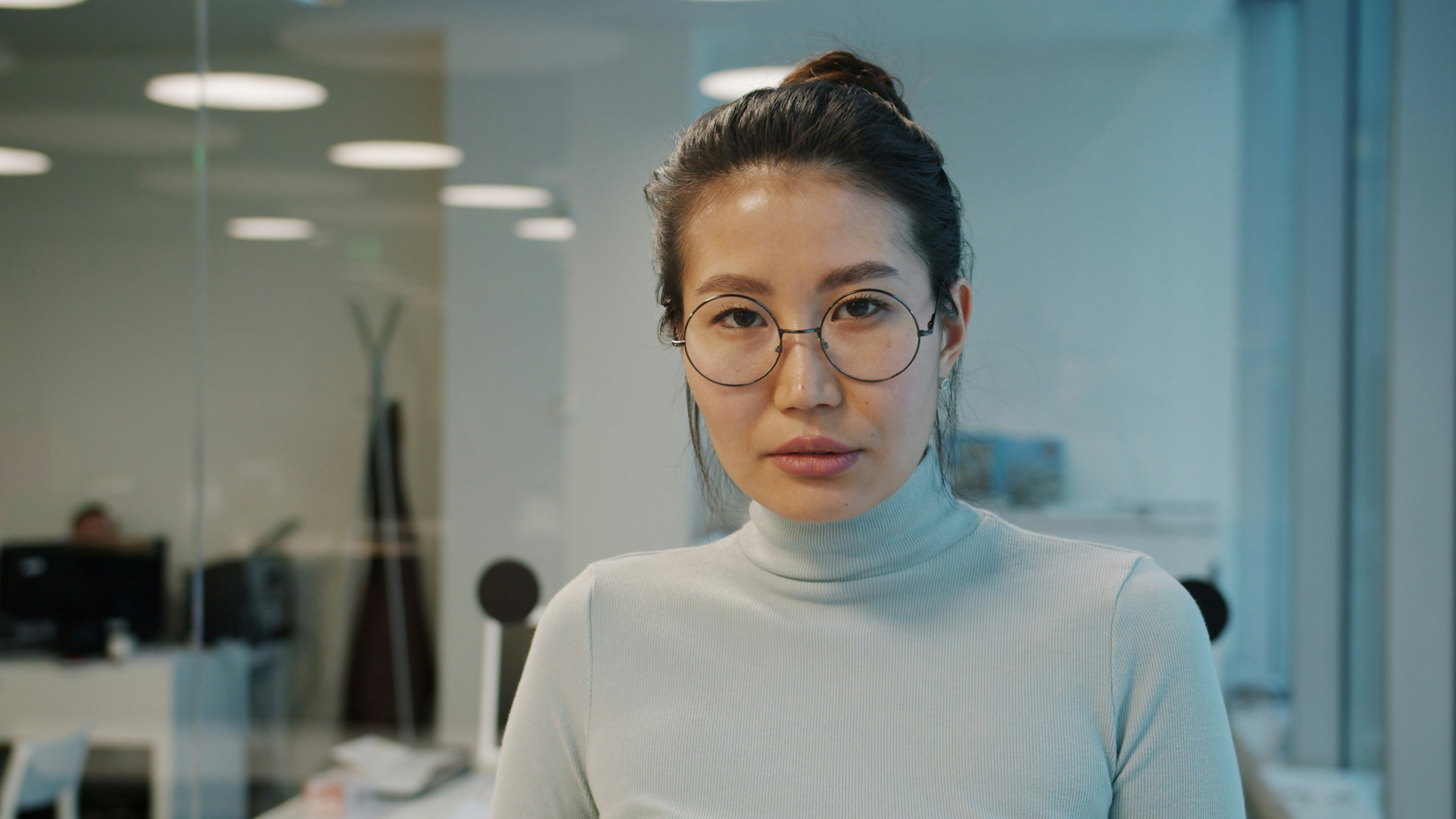 A woman with glasses wearing a turtleneck in an office.