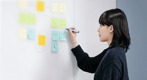 Person writing on colorful sticky notes attached to a wall in a modern workspace.