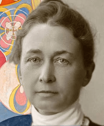 A woman with short curly hair wearing a black t-shirt looks into the camera.