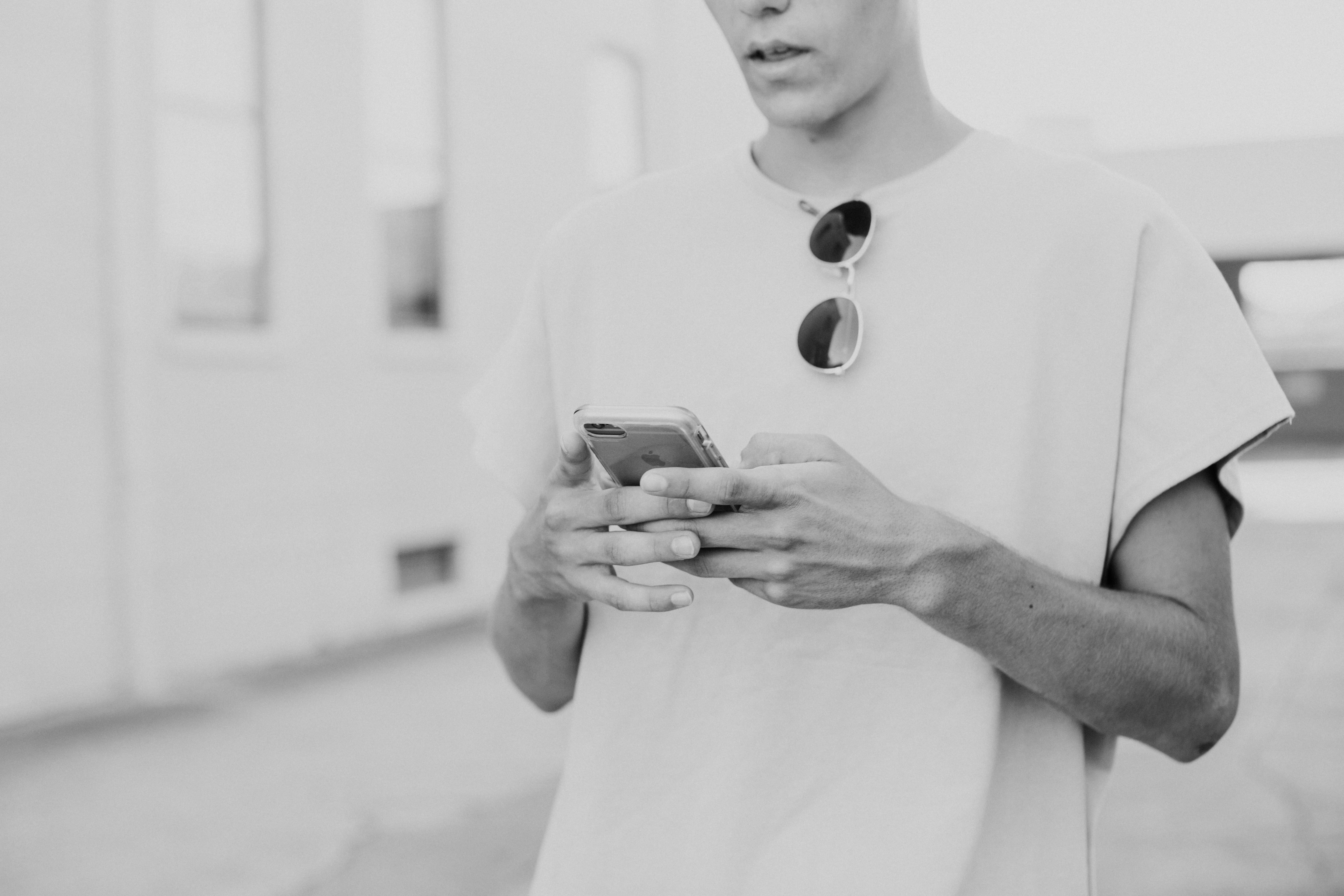 A person in a white shirt is holding a smartphone, focused on the device in a bright, minimalistic space.