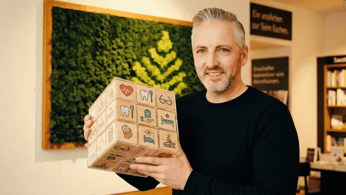 Hannes Weindorf hält einen Würfel mit verschiedenen Leistungen in der bKV in der Hand.