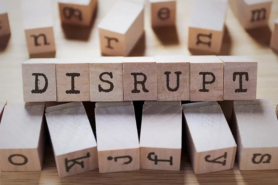 Wooden blocks arranged to spell the word "DISRUPT" with scattered letters around them on a wooden surface.