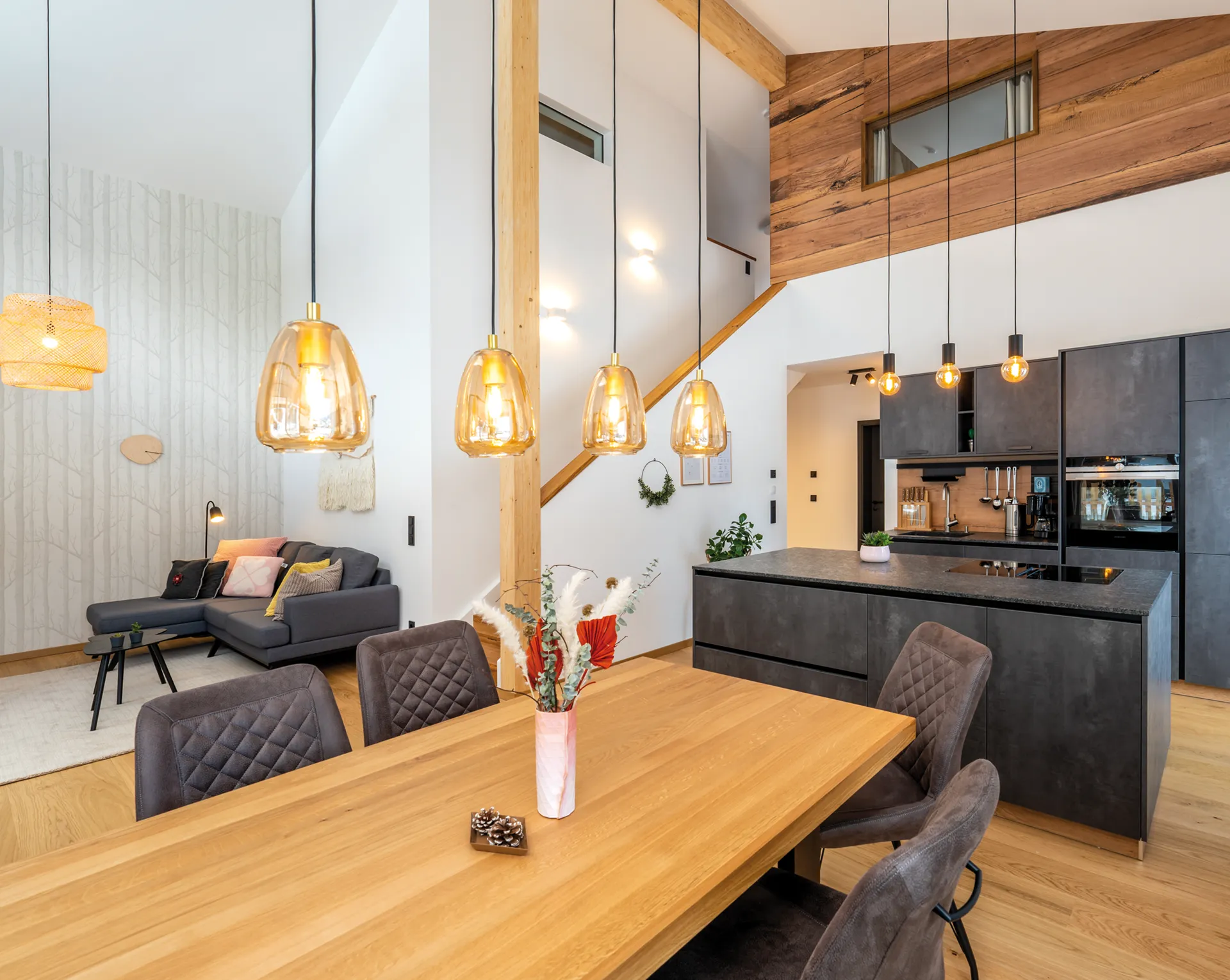 Moderner Essbereich und Küche mit Holztisch, gepolsterten Stühlen, Kücheninsel und Hängeleuchten unter einer hohen Decke.