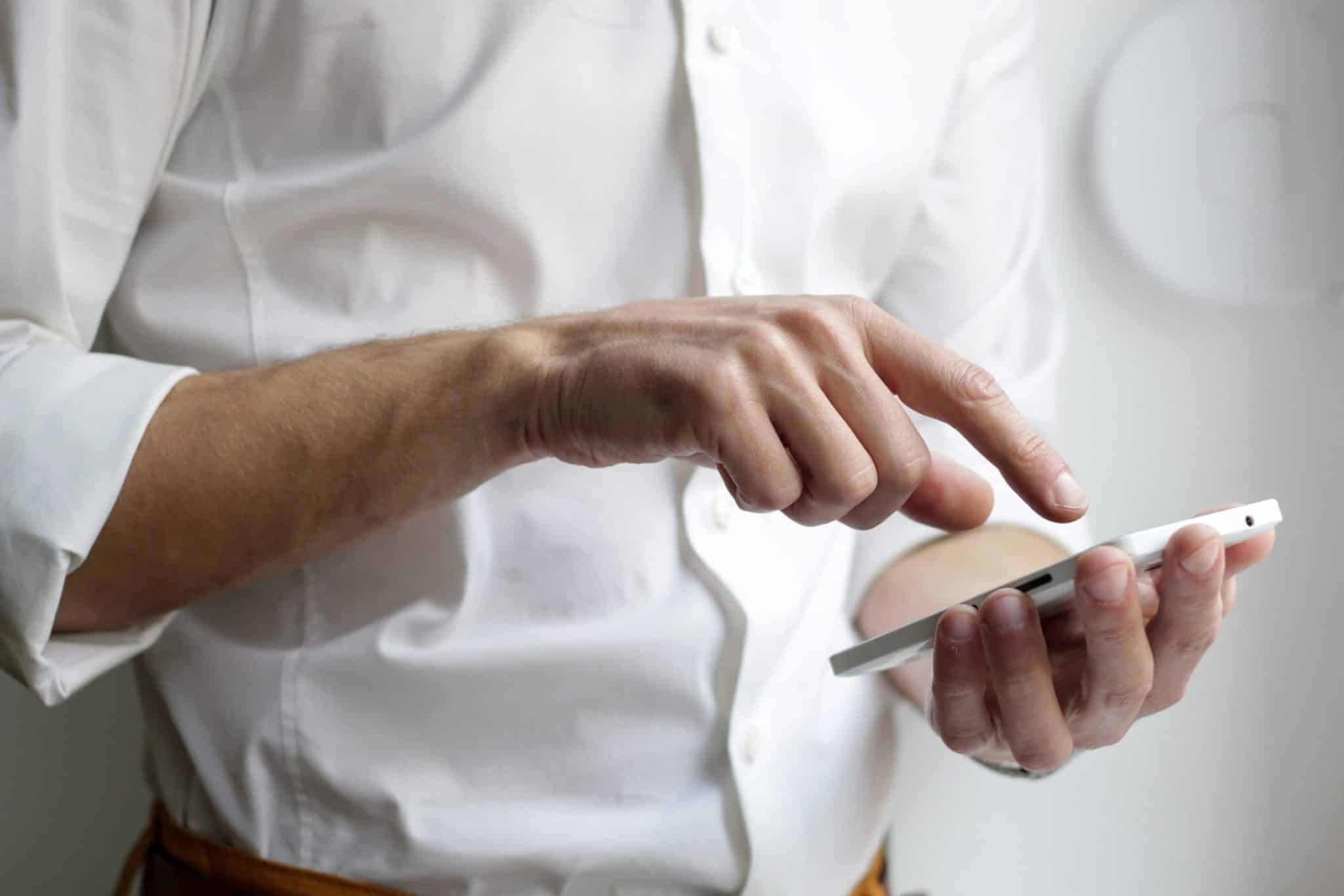 Person using smartphone, wearing white shirt, close-up on hands.
