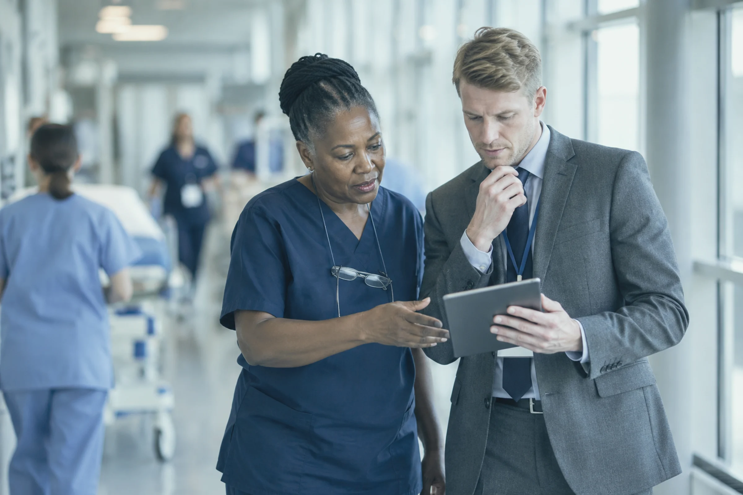 A ward manager and a consultant reviewing a tablet in a hospital corridor