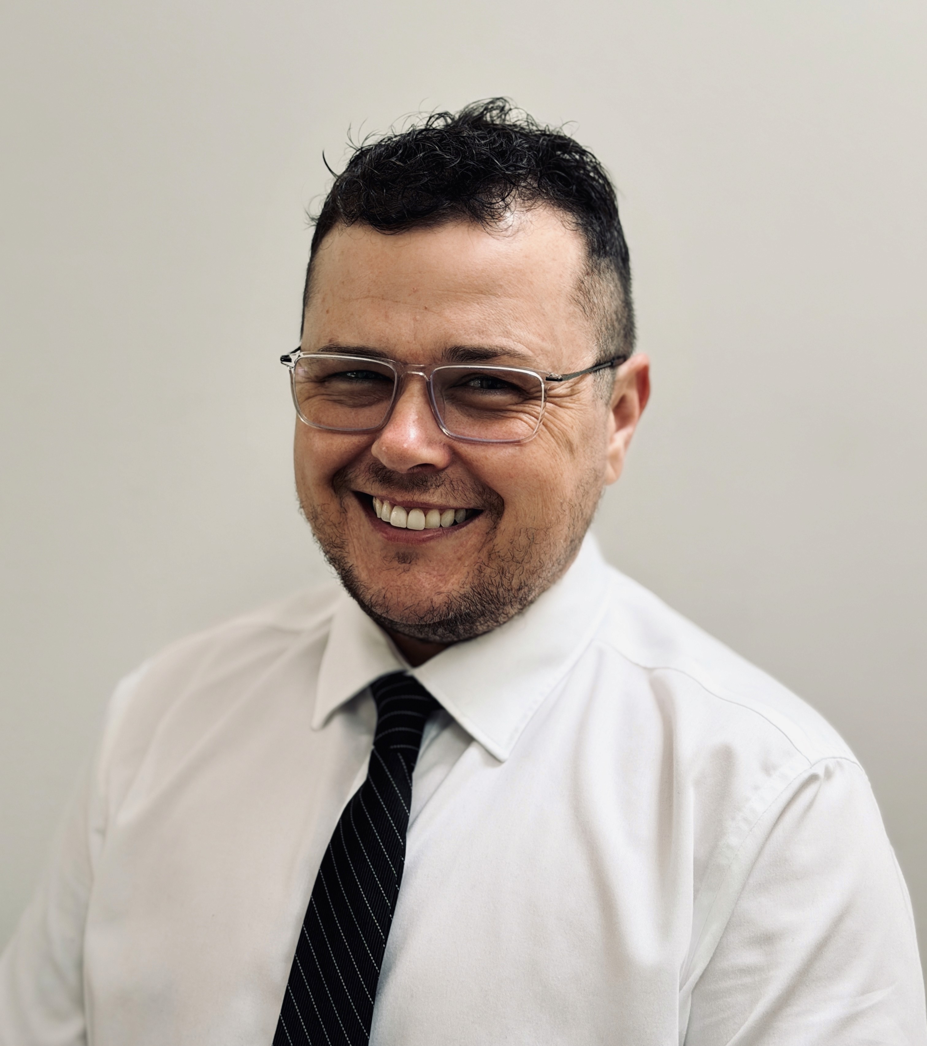 Smiling man in white shirt and black tie, with glasses, headshot