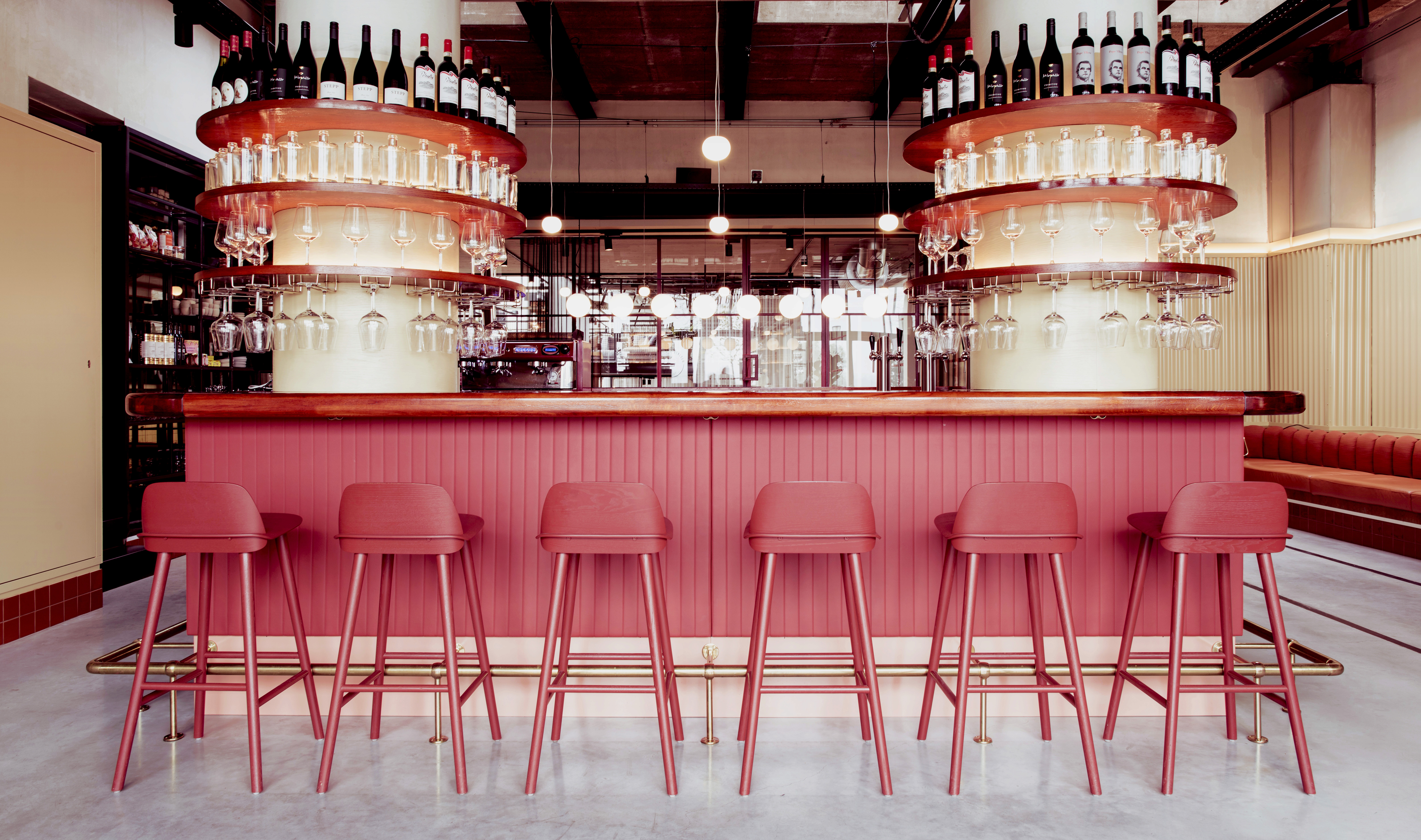 Bar met rode barkrukken en wijnflessen en glazen aan de bar, in een restaurant.