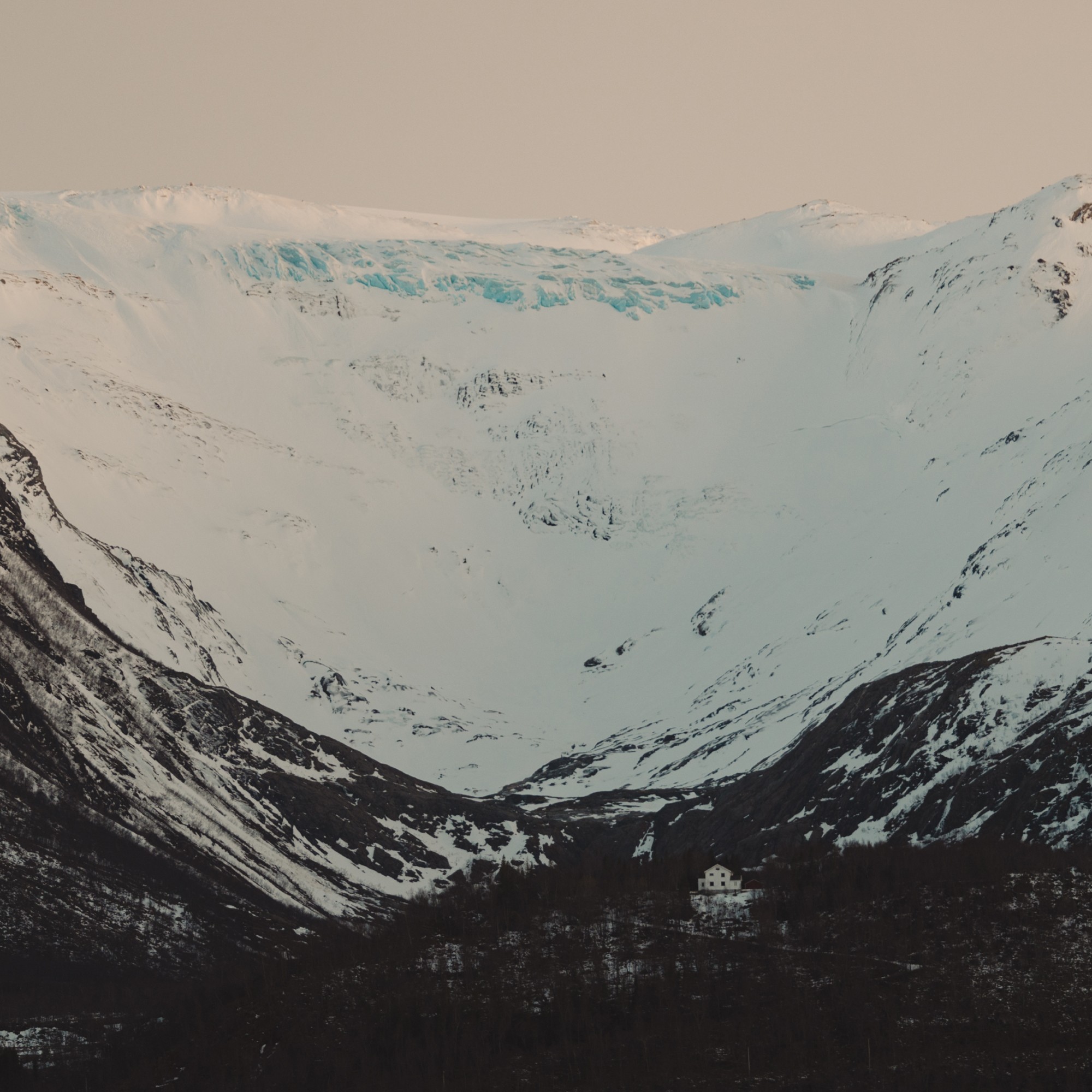 Snow-covered mountain range with glacier above a small remote house in Norway