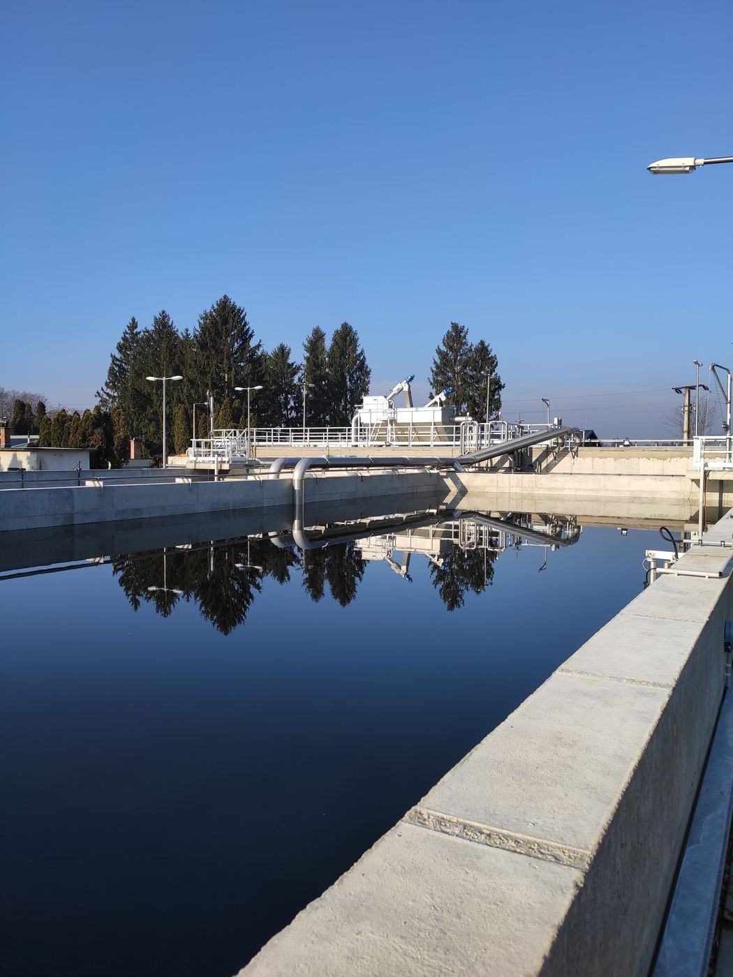 Still CYCLATOR basin reflecting the walkway and trees at the Lenti municipal wastewater treatment plant, Hungary