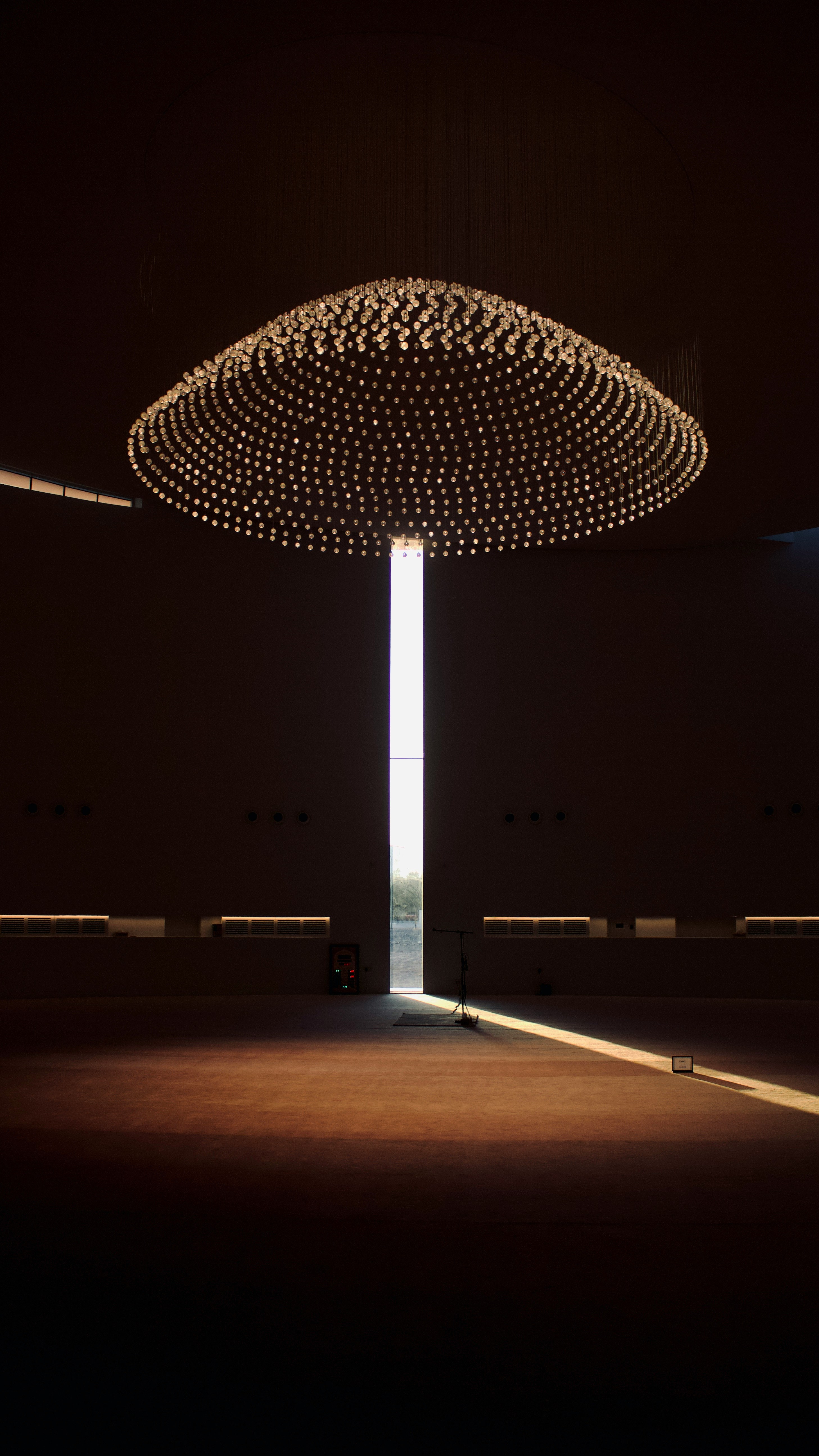 minimalist interior of a modern mosque, featuring a large circular crystal chandelier suspended above a dark prayer hall