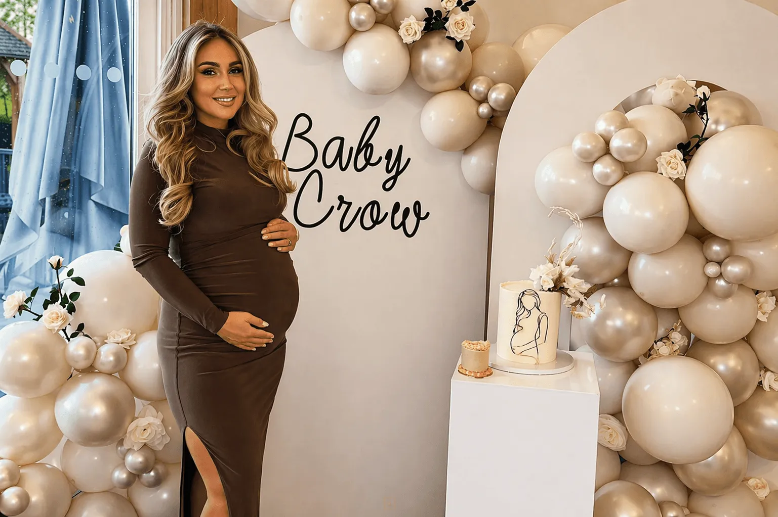 A woman in a fitted brown maternity dress smiles while holding her belly, surrounded by elegant white and silver balloons.