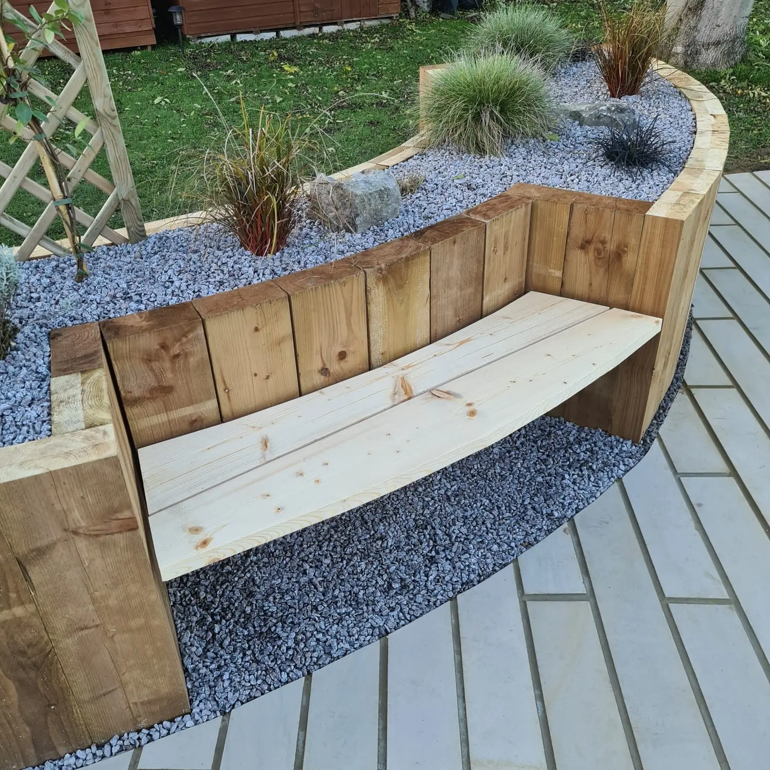 Curved wooden bench with stone top and potted plants, set in a well-maintained outdoor area.