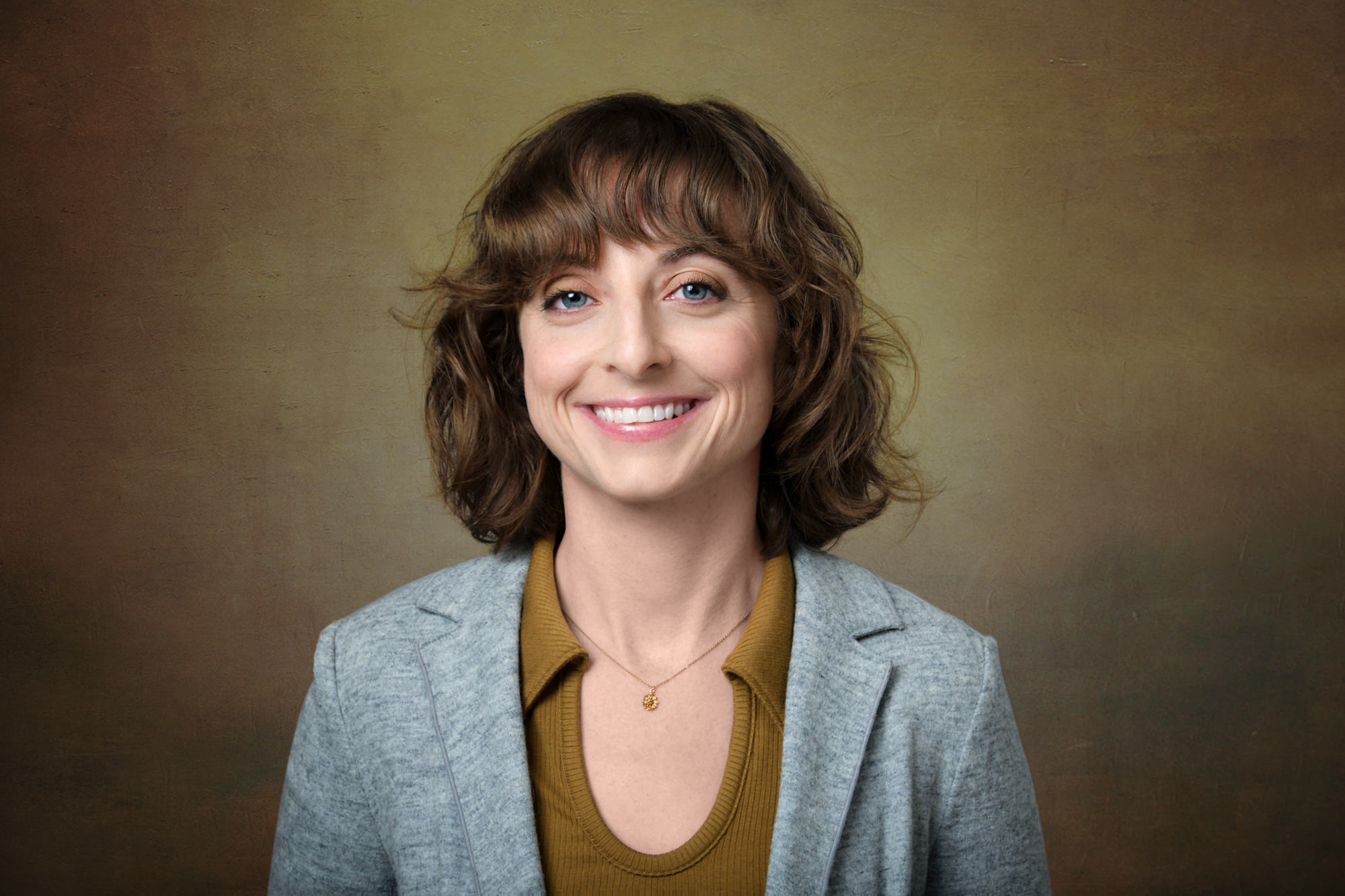 Professional portrait of white woman with curly brown bob in gray blazer and mustard top