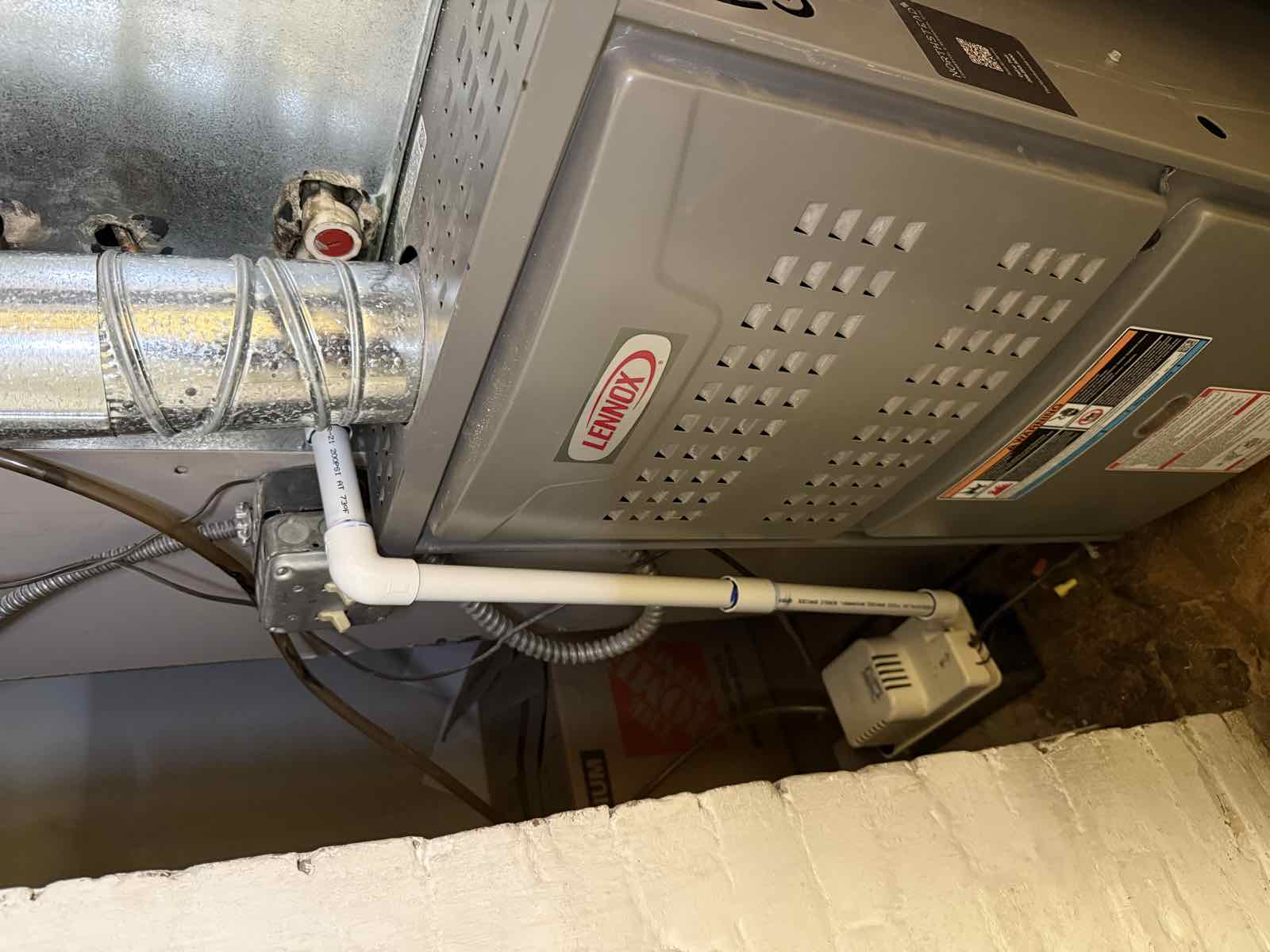 A white PVC condensate drain running from the top of a Lennox furnace down to a condensate pump on the floor.