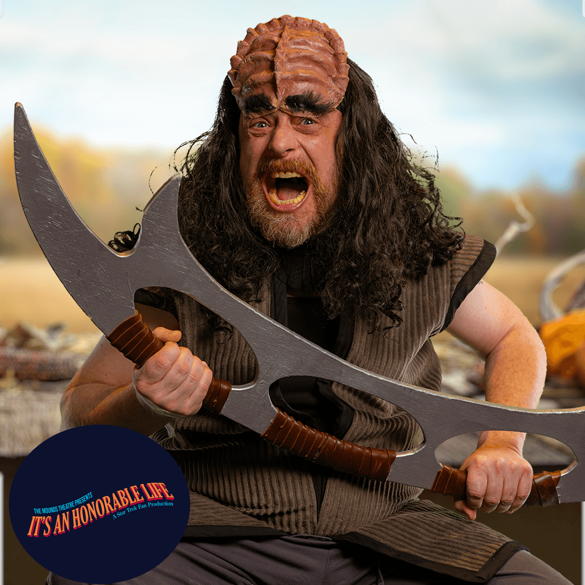 Portrait of a man in full Klingon cosplay armor holding a metallic bladed weapon on a stage set.