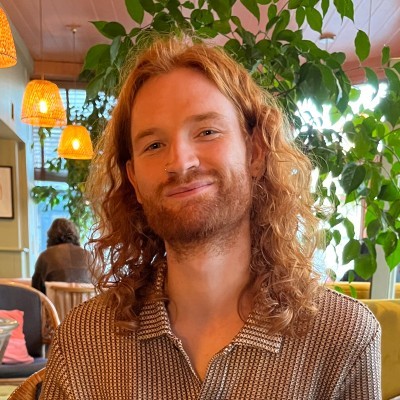 A portrait photo of Sam smiling with some plants behind him