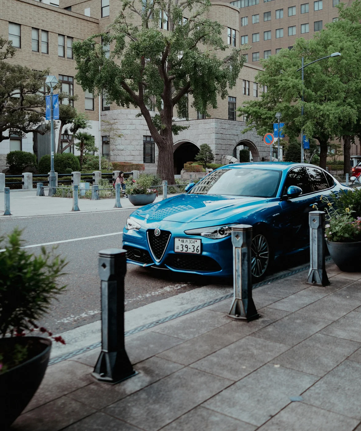 Une Alfa Romeo bleue garée dans une rue bordée d’arbres et d’immeubles. La berline sportive se détache nettement dans ce décor citadin élégant, soulignant son style raffiné et son dynamisme naturel.