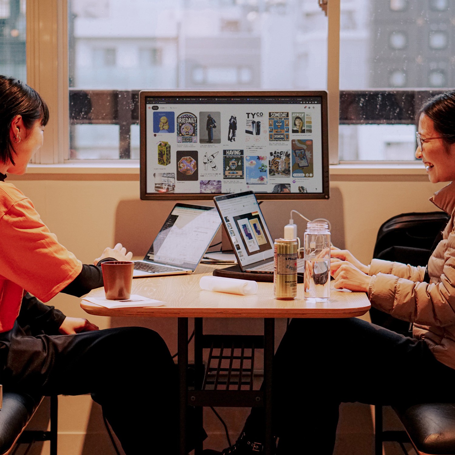 Black and white photo of two people looking at a computer screen with papers on wall
