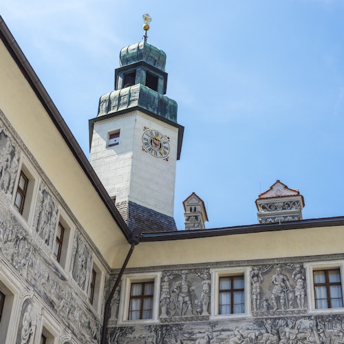 Edifício histórico com murais detalhados nas paredes e uma torre de relógio sob um céu azul.
