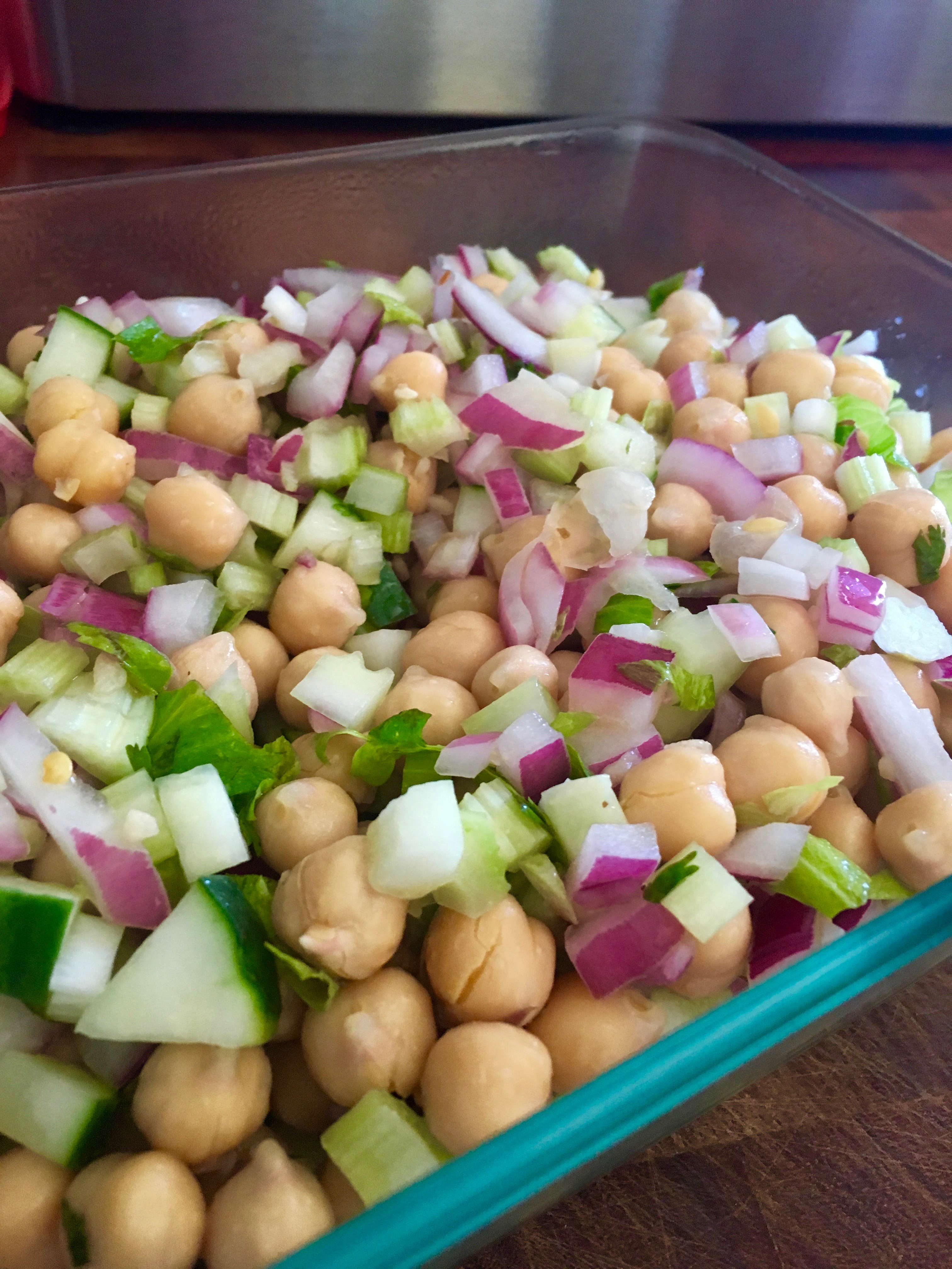 A glass dish filled with a fresh chickpea salad, featuring chopped cucumbers, red onions, and parsley, ideal for a healthy vegetarian meal.