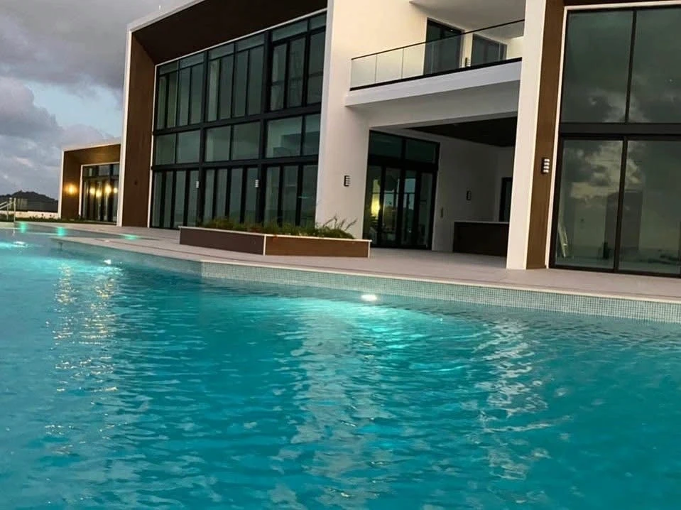 Lit pool deck at The Hill Residence in St. Lucia by Atelier International, framed by the tall glazed volume and covered outdoor living area.
