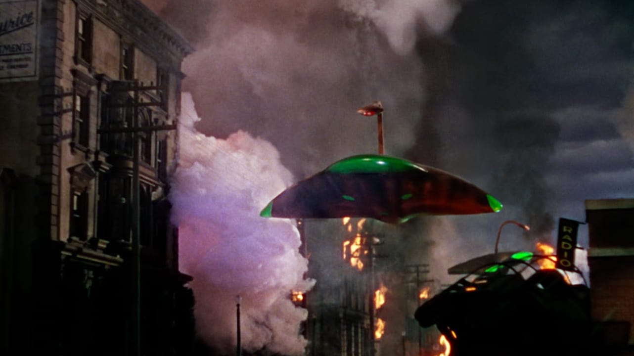 A scene depicting a dramatic urban landscape in chaos, with two UFOs emitting a green glow, towering over burning buildings. Smoke and fire fill the air, creating a sense of destruction and tension.