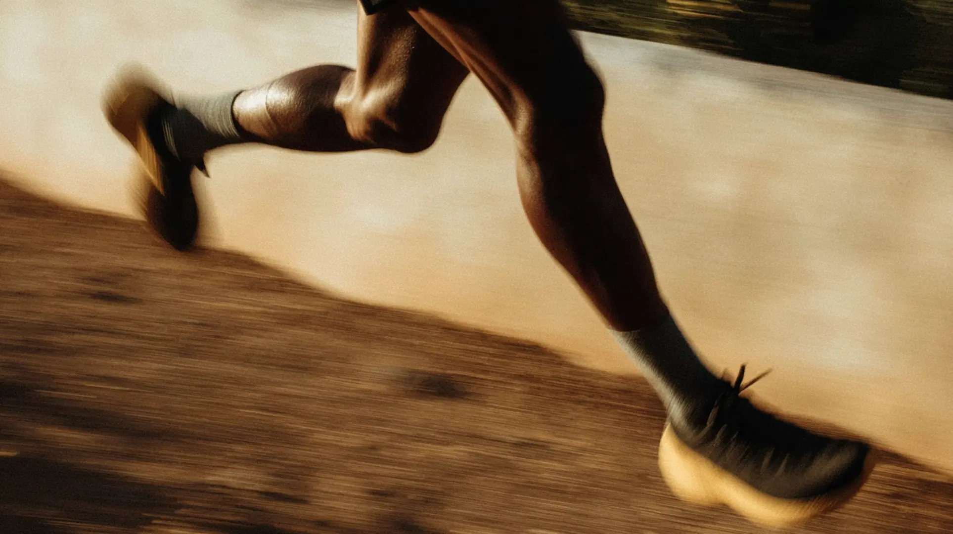 Muscular athlete sprinting forward with powerful motion, wearing light shorts and sunglasses against a plain neutral background.