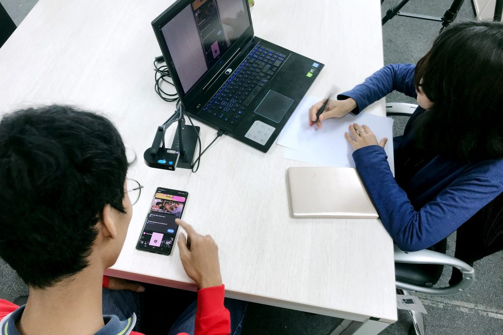Researcher taking notes while a participant tests an app on a smartphone during a usability test