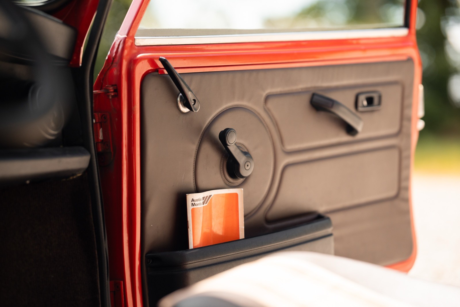 Close-up of a car door's interior, featuring a window handle and controls, with a vintage aesthetic.