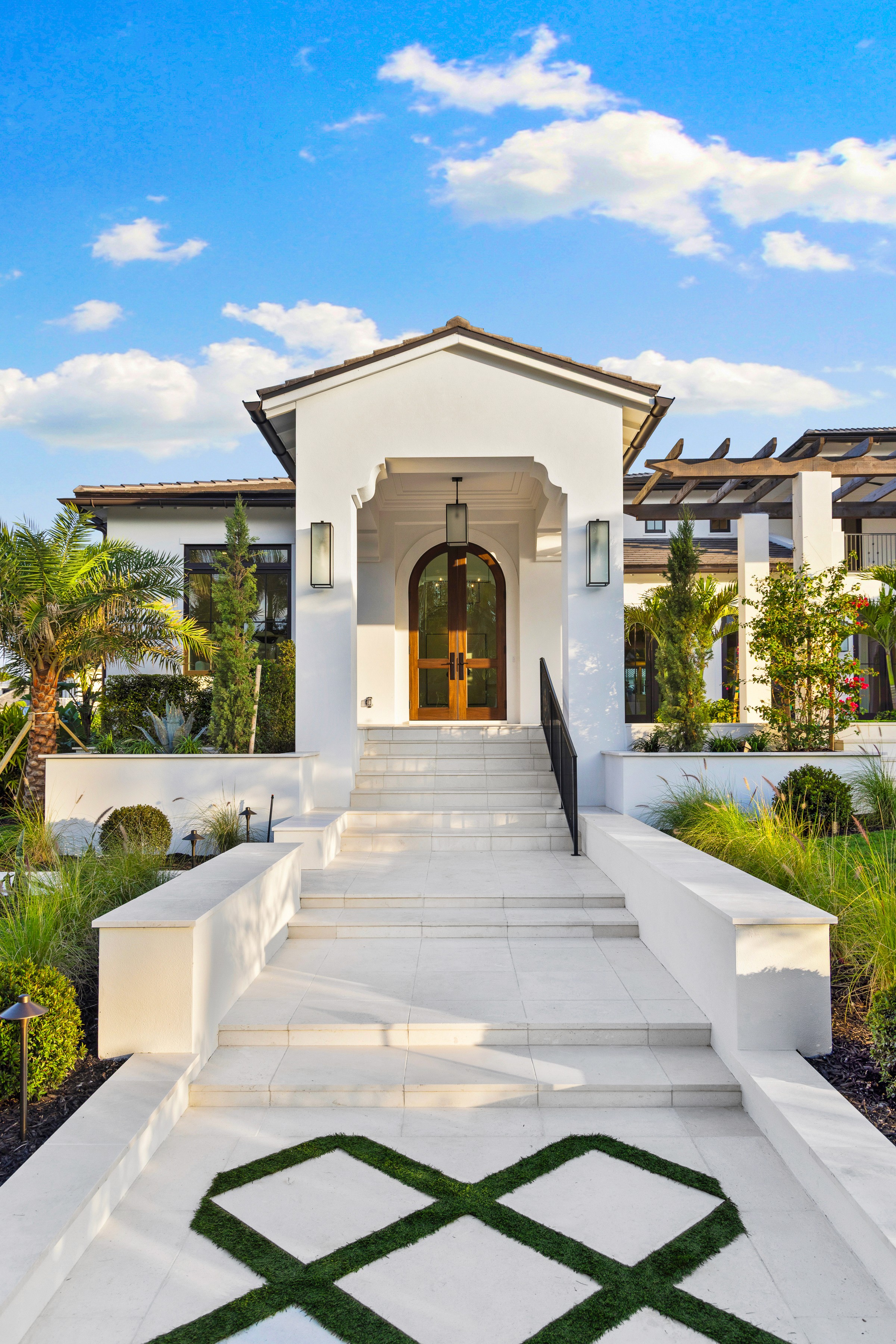 a british-indies styled entrance to a luxrious home with white steps and landscaping lining the pathway to the door