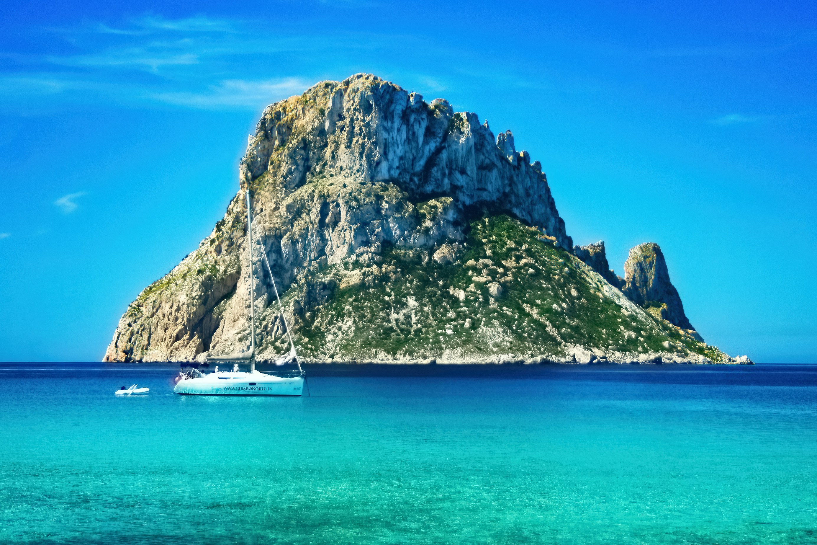 Large rocky island with green vegetation and clear blue water.
