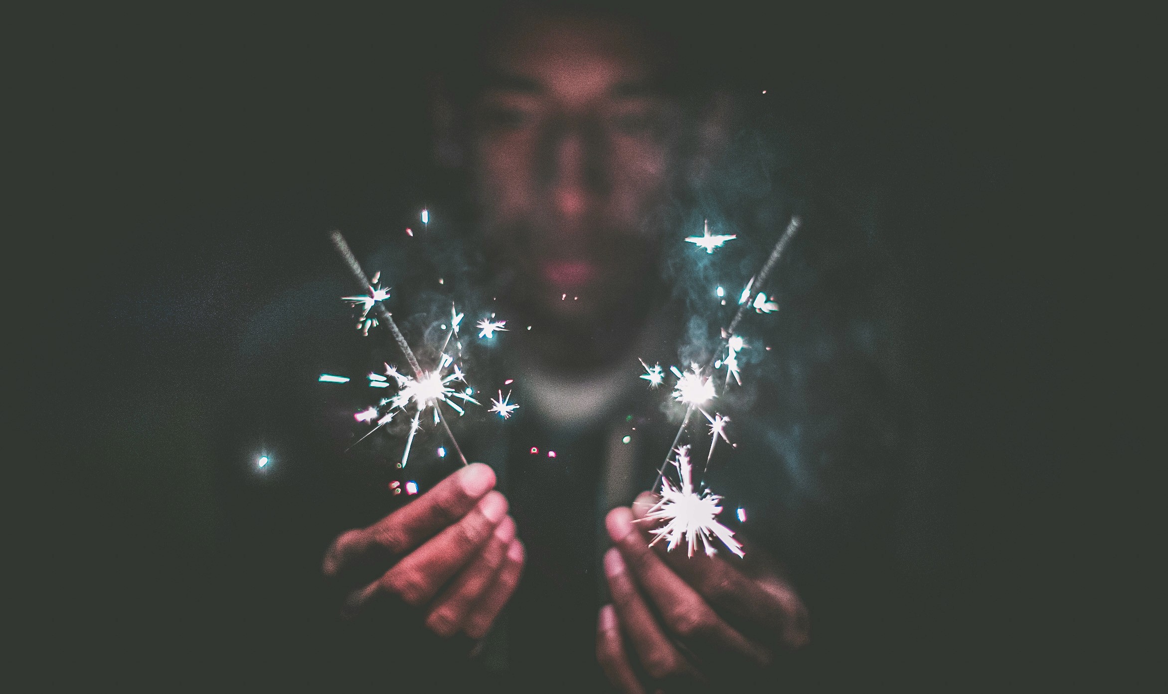 Man holding to sparklers, his face blurred in the back