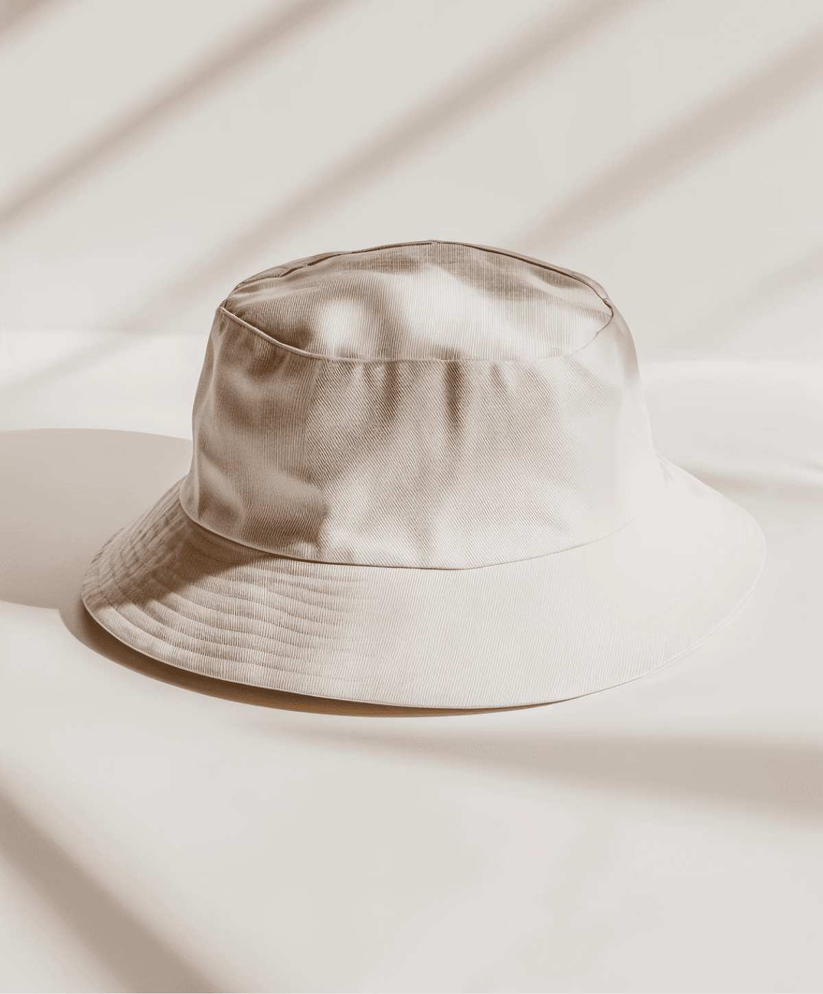 Minimalist beige bucket hat made of soft fabric, placed on a neutral surface with subtle shadow patterns