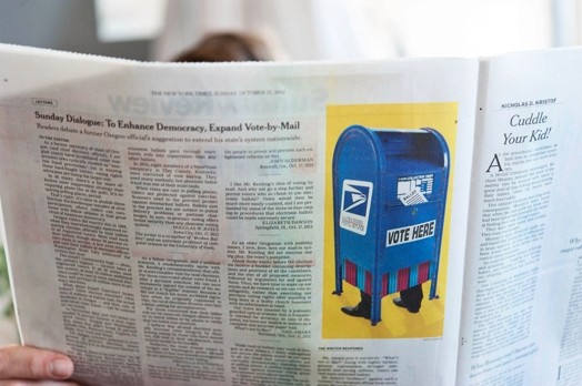 A photo of a newspaper with a picture of a blue mailbox with feet on it.