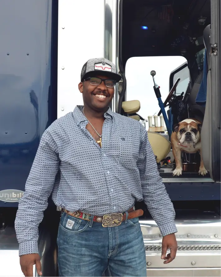 A male truck driver and his bulldog Ms. Chunky posing together by the cab of his truck