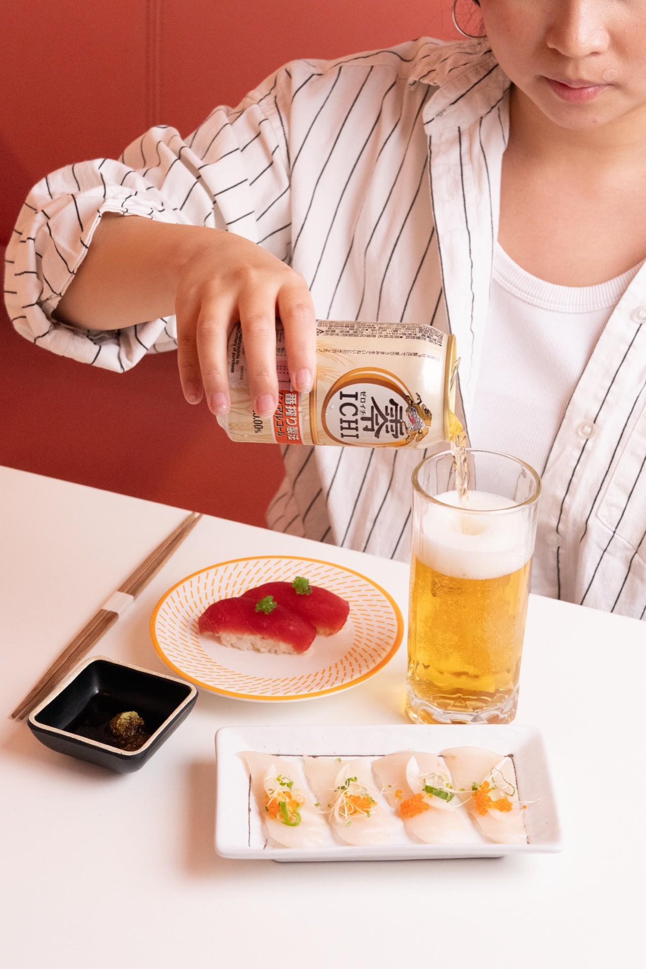 Person pouring beer beside sushi dishes