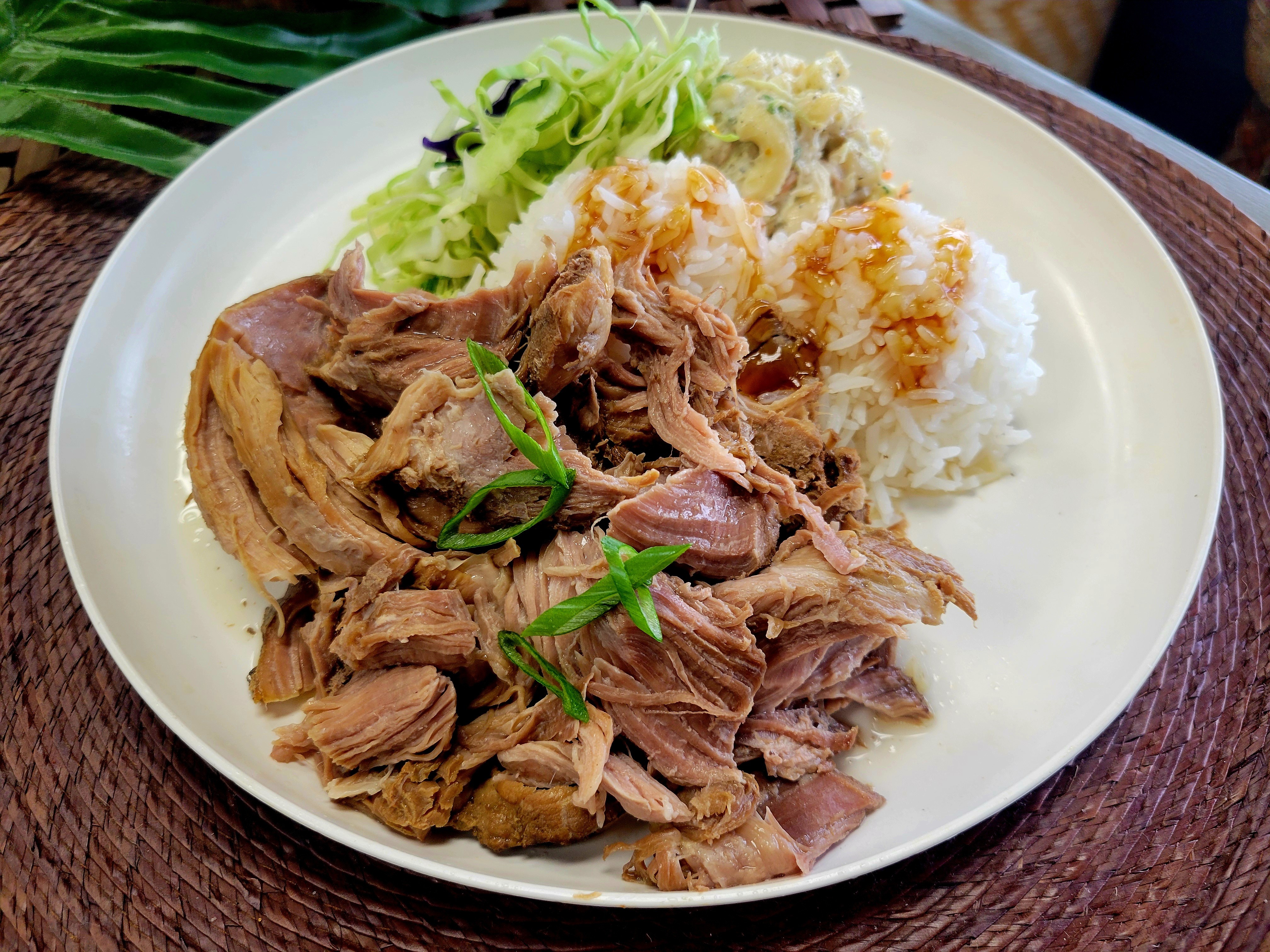 A traditional Hawaiian plate lunch featuring a generous mound of smoky, shredded Kalua Pork, two scoops of white rice, macaroni salad, and fresh Asian slaw.