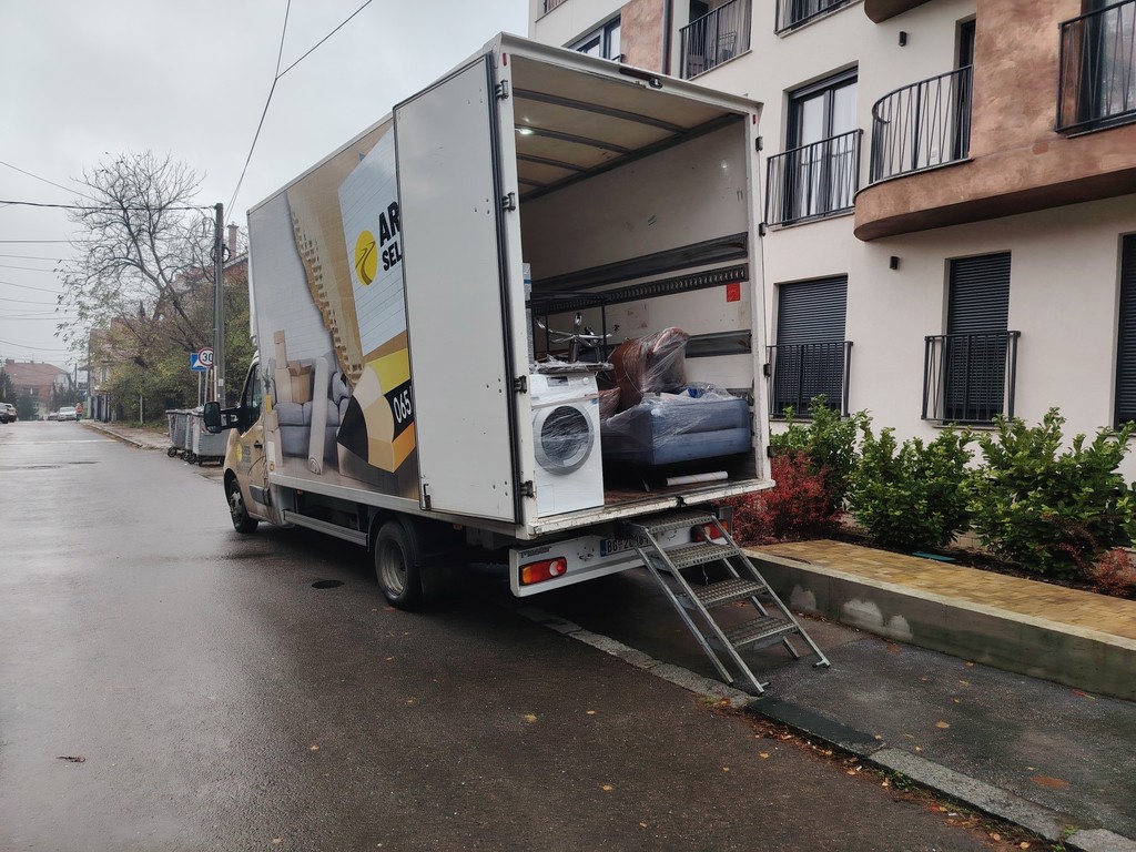 Otvoren kamion Ares selidbe parkiran ispred zgrade, napunjen zapakovanim nameštajem i tehnikom.