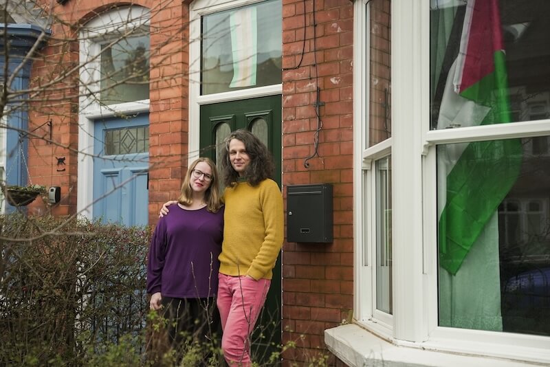 A couple standing and smiling in front of their home.