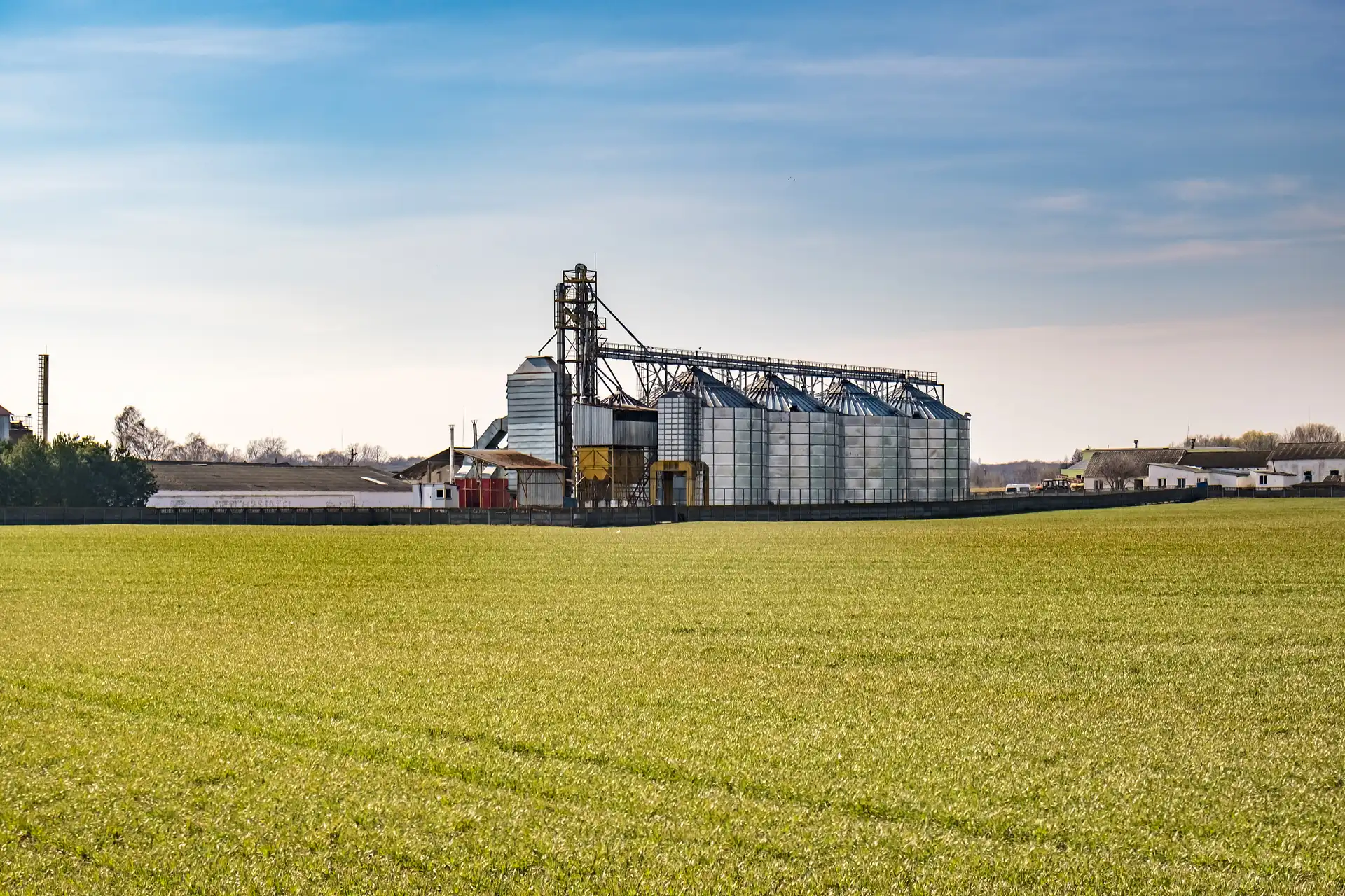 An aerial view of a cargo train with tanker cars moving past agricultural fields, including a golden field above and green crop rows below.