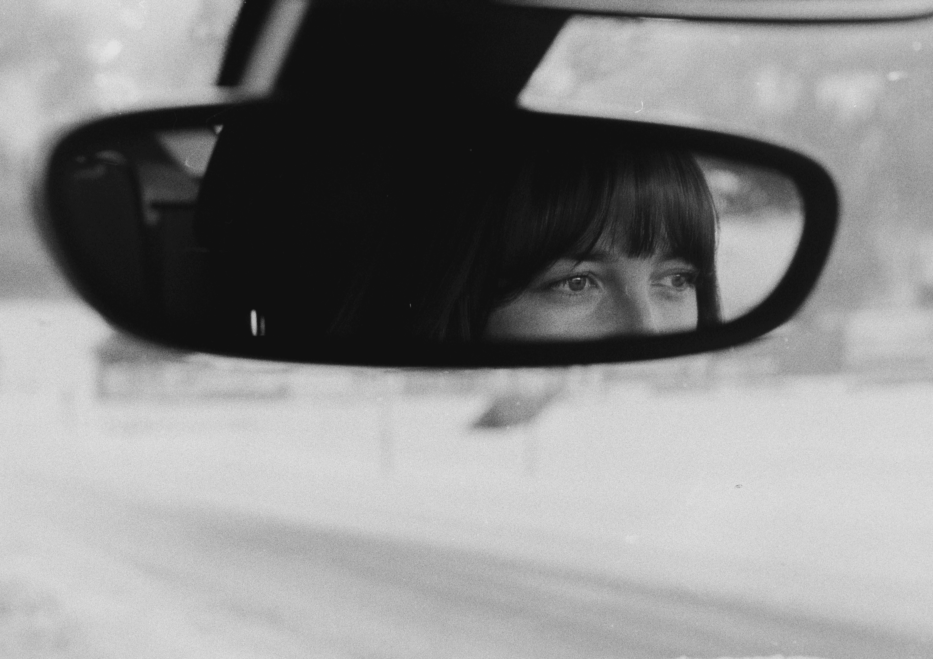 A thoughtful young person with dark hair gazes to the side, captured in soft black and white lighting.