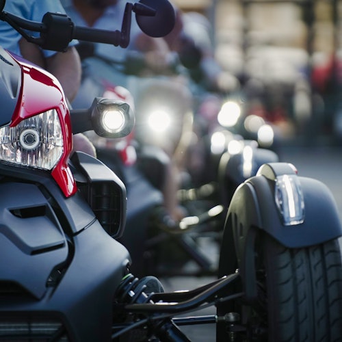 Close-up of a row of three-wheeled motorcycles or trikes parked closely together, with headlights and front wheels visible.