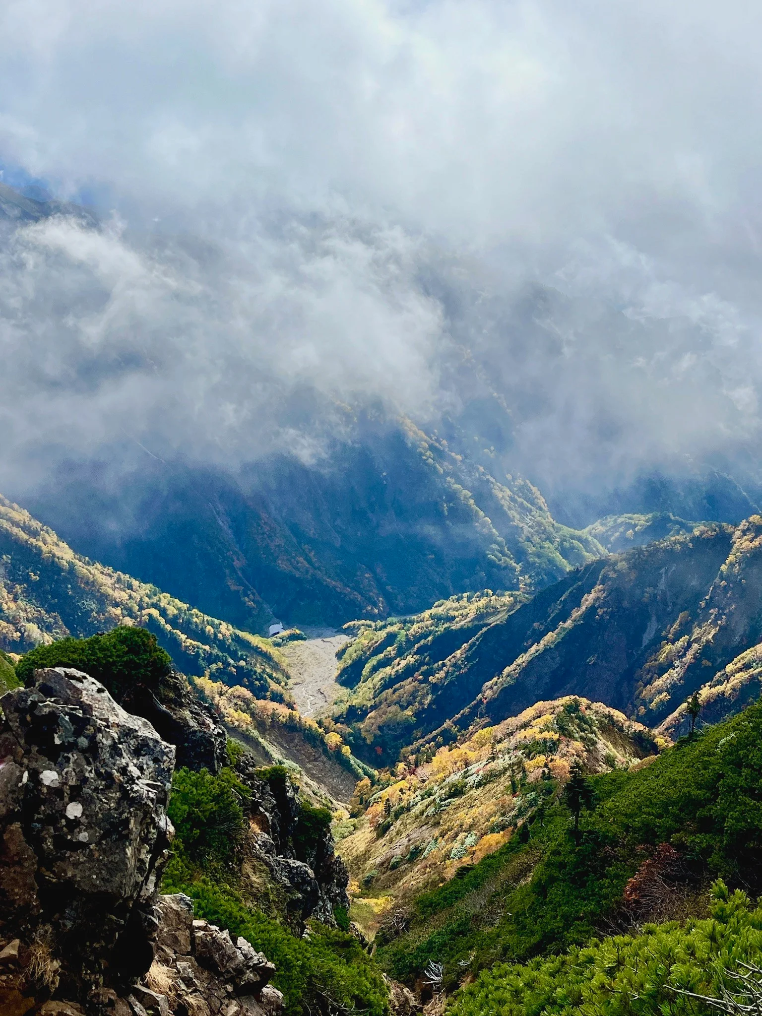 A scenic mountain landscape with rolling hills in Hakuba, lush greenery, and clouds partially obscuring the peaks.