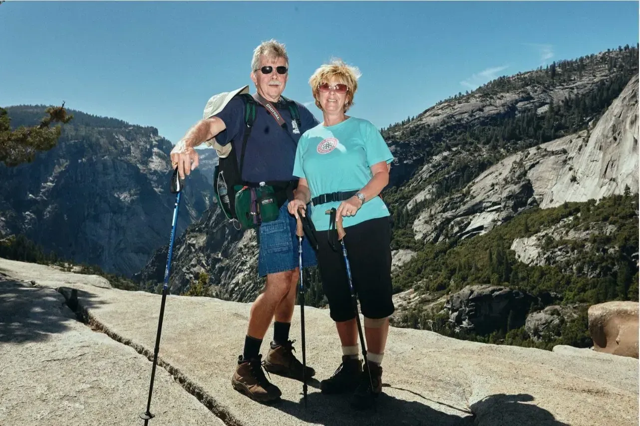 Two hikers with trekking poles posing on a mountain trail.