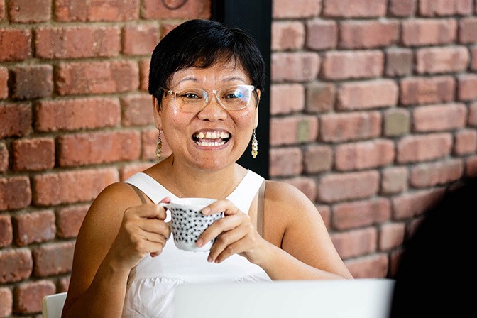 A frontal image of our team member, Mai, holding a cup in her hands and smiling at a person in front of her.